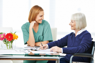 Smiling senior woman solving crossword puzzles next to nurse in nursing home